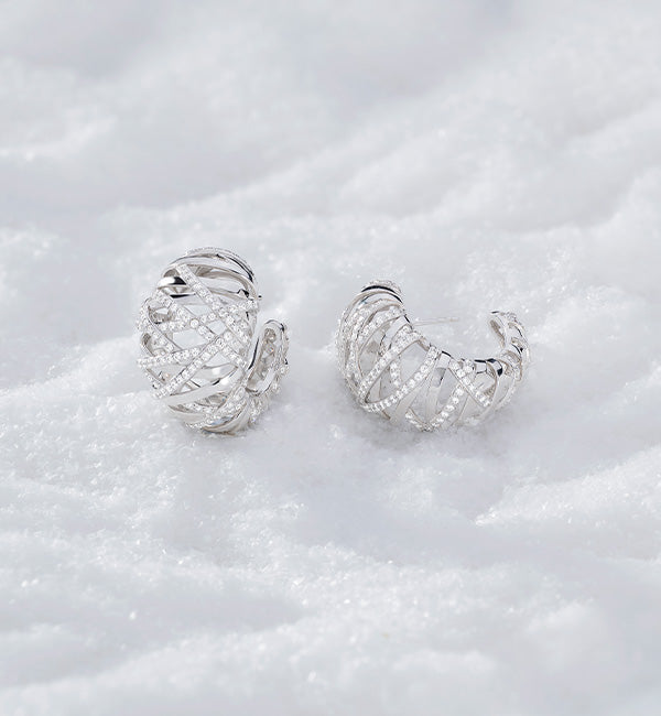 Pair of APM MONACO silver hoop earrings on a white textured surface